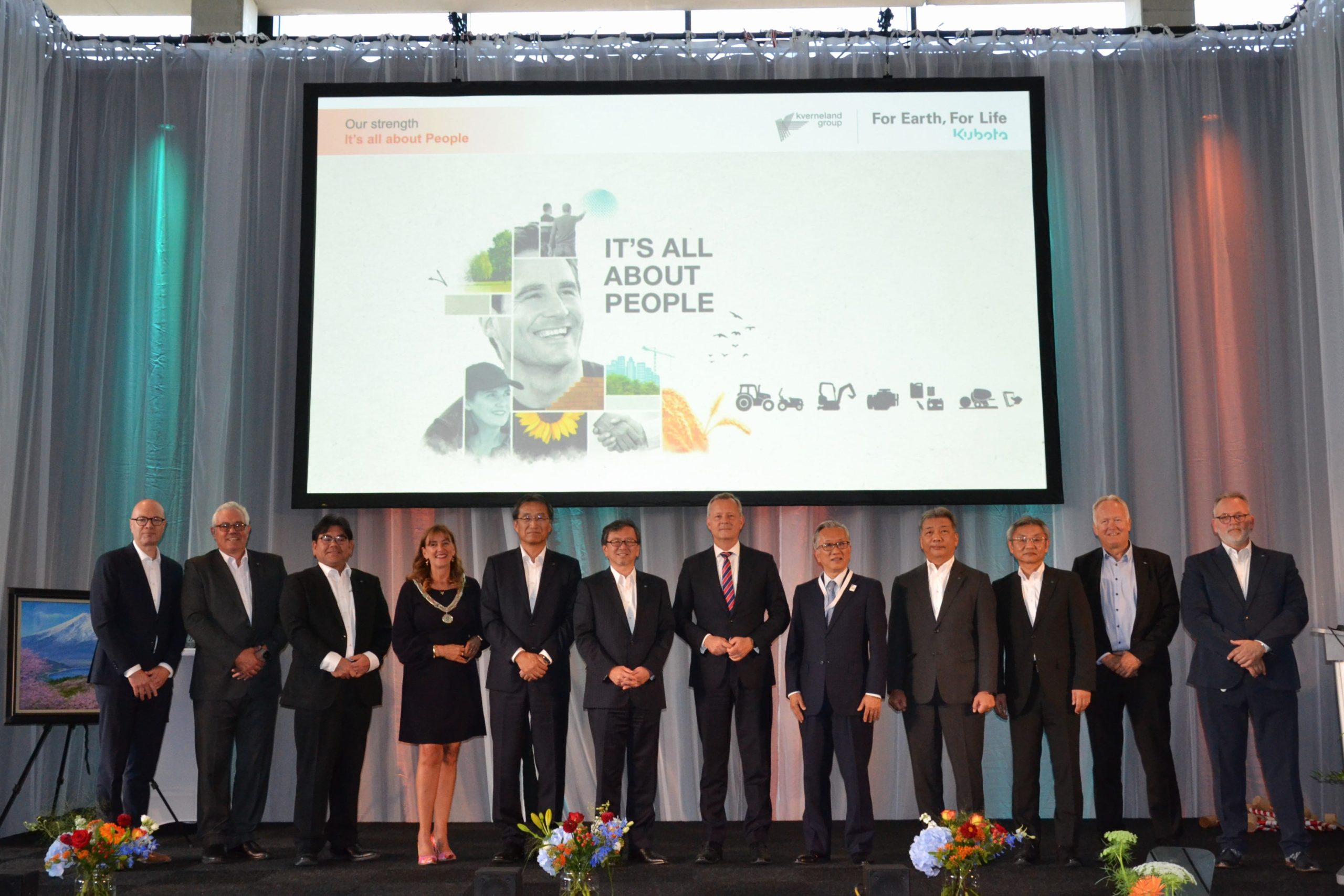 Image showing the Honored guests attending the European Kubota Headquarters opening ceremony on stage in front of a screen.